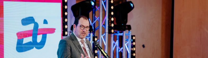 João Costa speaking on stage in front of a sign saying Poland 25