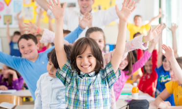 A group of children in a classroom wearing brightly coloured clothes and waving their arms in celebration