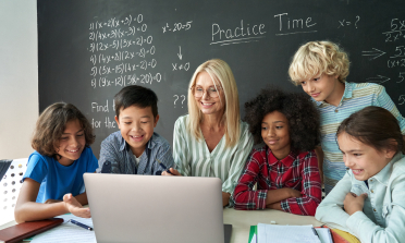 A teacher sits in front of a laptop, surrounded by six learners