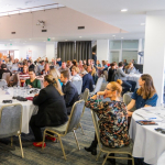 Groups of people sit around tables in a conference room