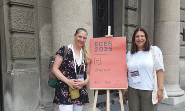 Two people stand either side of a sign that reads 'ECER 2025 check in'